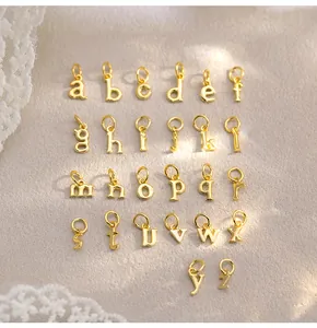 Vue macro détaillée de 26 breloques lettres minuscules en or poli sur un tissu en dentelle