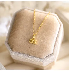 Gros plan d'un collier doré avec pendentif lettre 'm' minuscule sur boîte velours