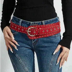 Cintura punk in pelle rossa con borchie e occhielli d'argento su jeans blu denim