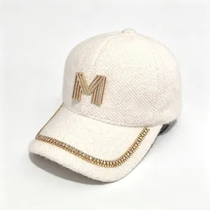 Close-up of the rhinestone M logo and chain detail on a warm mink velvet baseball cap