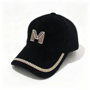 Close-up of black faux fur baseball cap with rhinestone M logo and chain brim detail.