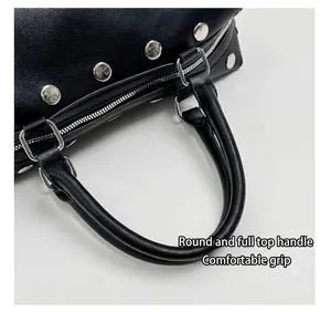Close-up of black riveted handbag showing comfortable rounded top handles detail.