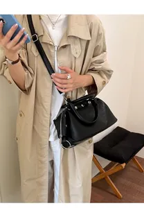Detailed view of the retro black rivet handbag styled with a beige trench coat outfit