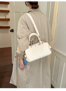 Detailed side view of a stylish vintage beige rivet shoulder bag carried by a model in a trench coat