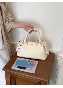 Close-up of retro cream handbag with silver rivet details on wooden nightstand