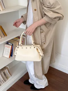 Casual cream-colored vintage handbag featuring silver rivets held by a model in a studio.