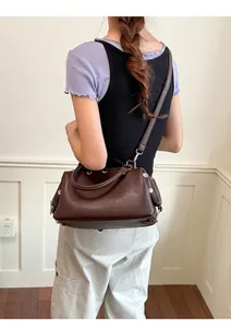 Close-up of a vintage brown rivet handbag carried by a woman in casual attire.