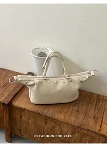 Vintage-style cream tote bag with elegant rivet details on a rustic wooden chest.