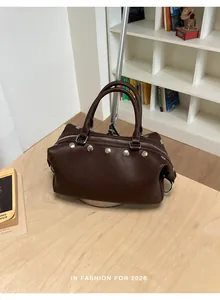 Vintage dark brown faux leather handbag with silver rivets on a minimalist wooden table