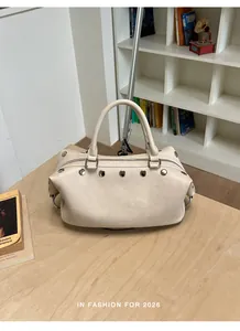 Detail view of a stylish beige rivet handbag on a wooden table with books in background