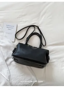 Detailed top view of a black retro rivet handbag with crossbody strap on white fabric