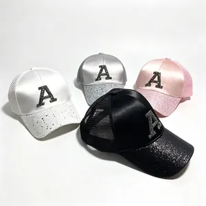 Dettaglio di cappellini trucker in raso con lettera A in strass e visiera glitter.