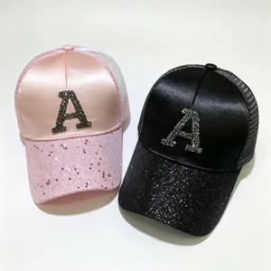 Dettaglio dei cappellini da baseball in raso e mesh con lettera A di strass rosa e nero.