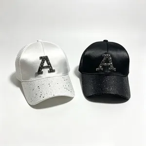 Dettaglio di cappelli da baseball in raso con lettera A in strass e visiera di paillettes