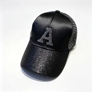 Dettaglio cappellino di raso nero con lettera A di strass e visiera di paillettes.