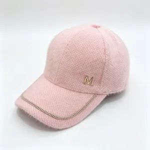 Detail view of a pink fuzzy mink velvet baseball cap with rhinestone M logo and chain trim