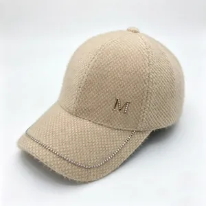 Detail of mink fleece baseball cap with rhinestone M-logo and sparkling chain brim.