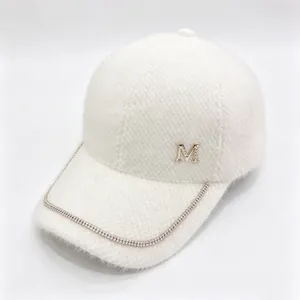 Close-up of a white faux fur baseball cap with rhinestone chain and metal M logo.