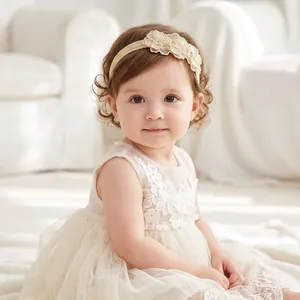 Sweet floral lace headband on a baby girl with curly hair in a white dress.