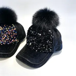 Nahaufnahme schwarzer Samt-Baseballcaps mit Glitzer-Pailletten und flauschigen Bommeln
