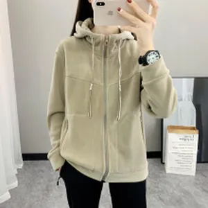 Detailed view of a cozy beige fleece zip-up hoodie worn in a casual indoor setting.