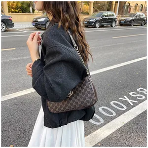 Detailed view of a woman wearing a monogrammed crescent shoulder bag in a street setting