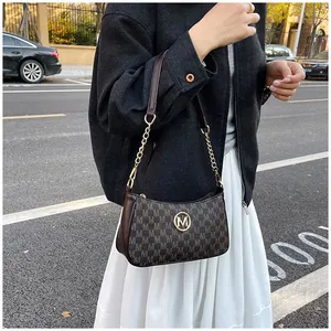 Detail shot of a stylish brown underarm bag featuring an M-letter print and golden hardware