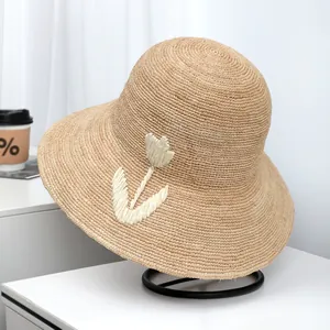 Close-up of fine raffia straw sun hat with woven flower detail on white surface stand