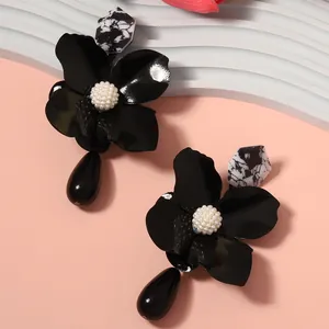 Close-up of black metal flower earrings with white pearl center and marble geometric studs.