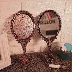 Vintage handheld makeup mirror with intricate floral engraving in rose gold and bronze
