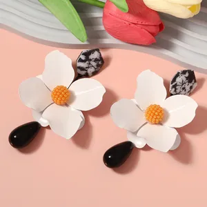 Detail showing oversized white metal flower earrings with black teardrop pendants.