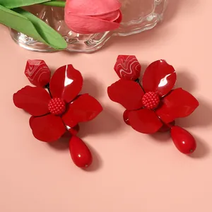 Close-up of large red metal flower earrings with water drop pendants and matte finish.