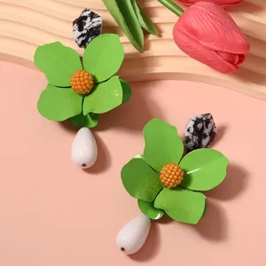 Close-up detail of oversized green metal flower earrings with white teardrop pendant