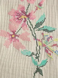 Close-up of intricate colorful floral cross-stitch embroidery on a beige textured fabric vest