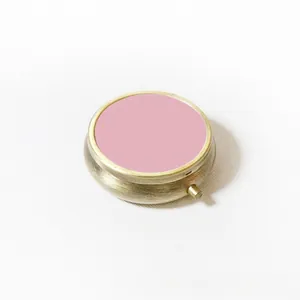 Détail d'une boîte à pilules ronde en métal avec couvercle rose et finition bronze