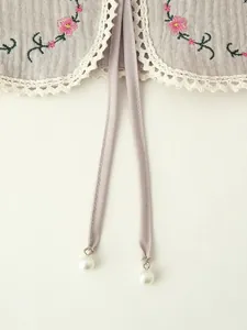 Detailed view of pink flower embroidery and white lace trim on a retro gray vest
