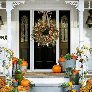 Decorative autumn pomegranate wreath with green leaves and red fruit on a white house door