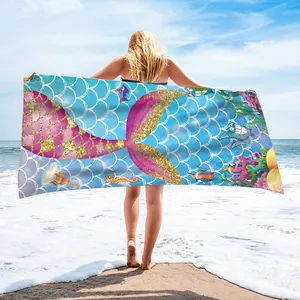 Colorful mermaid tail microfiber beach towel held by a woman on a sunny beach shore