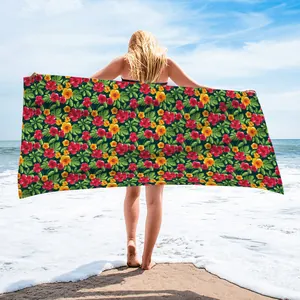 Model holding a microfiber beach towel with a vibrant tropical floral pattern on a beach.