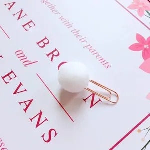 Close-up of cute rose gold paper clip with decorative white fluffy pom-pom detail
