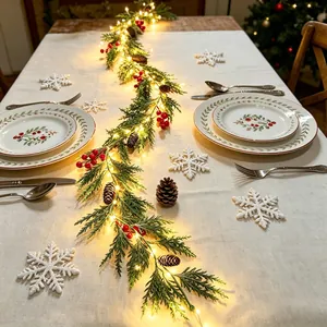 Festliche Weihnachtsgirlande mit warmen LED-Lichtern, roten Beeren und Tannenzapfen auf Tisch.