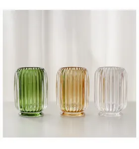 Detail view of three ribbed glass makeup brush holders in green, amber, and clear.
