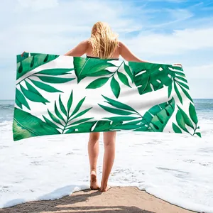 Large microfiber beach towel with green tropical leaf print held by a woman at beach