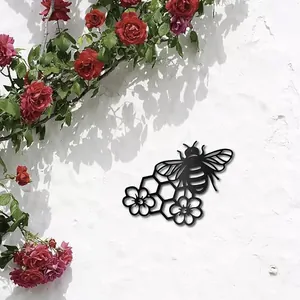 Decorative black metal bee and honeycomb wall art hanging on white wall with roses