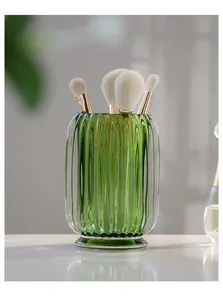 Close-up of a green ribbed glass holder with makeup brushes in a bright setting.