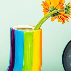 Makroansicht einer lebendigen, regenbogengestreiften Deko-Vase aus Harz mit Gerbera-Blumen