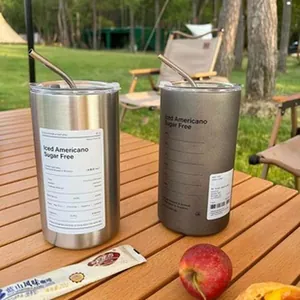 Zwei isolierte 304-Edelstahlbecher mit Strohhalmen auf einem hölzernen Camping-Tisch.