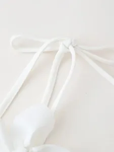 Close-up detail of tied bow straps and delicate fabric flower on a white crop top