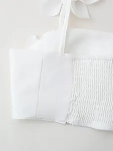 Close-up view of a white fashion crop top featuring smocked back detail and tie strap