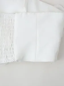 Detailed macro view showing white fabric smocking and stitching texture on a crop top.